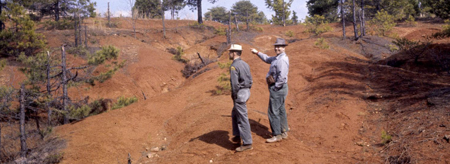 Two men stand on a hillside with washed-out soil visible